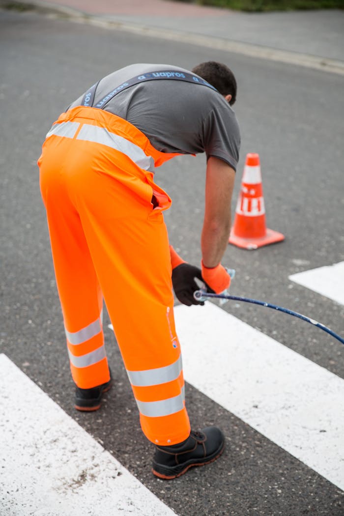 A worker in a fluorescent suit performing road maintenance at a crosswalk with cones.