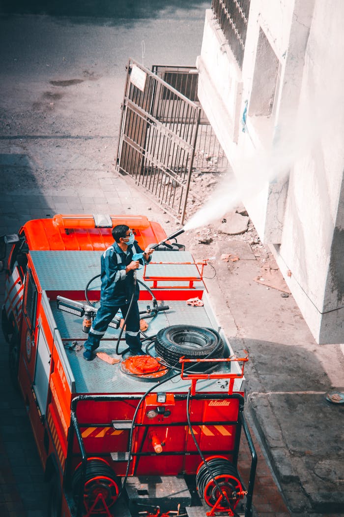 High-angle view of a firefighter sanitizing a building exterior during the pandemic from a fire truck.